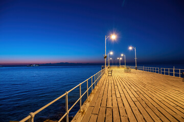 A pier extending into the sea with bright lanterns on the Limassol promenade at night, Cyprus