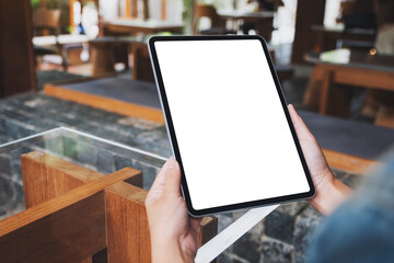 Mockup image of a woman holding digital tablet with blank white desktop screen in cafe