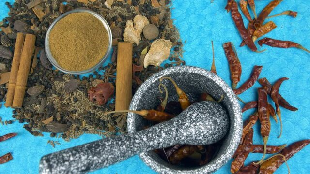 A bowl of Garam Masala powder is placed with various other Indian spices. A mortar-pestle with a few dried whole red chilies is kept on a table with a blue mat - food preparation  grinding  flavorful