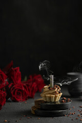 Obraz na płótnie Canvas Little cake with candle and smoke with red roses on black table. Mystic dramatic birthday concept. Dark mood greeting birthday card.