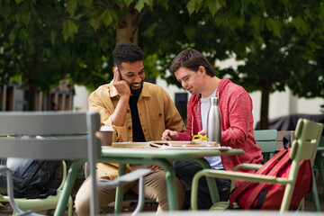 Young man with Down syndrome with his mentoring friend sitting outdoors in cafe and studying.