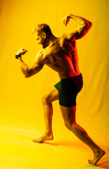 Fototapeta na wymiar muscular man in blue shorts posing shows, straining his muscles. yellow and red highlights on the face and background