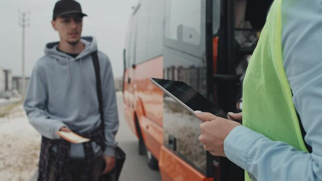 Midsection shot of unrecognizable female ticket controller in acid green vest standing at bus entrance door scanning electronic and printed tickets of passengers getting on bus