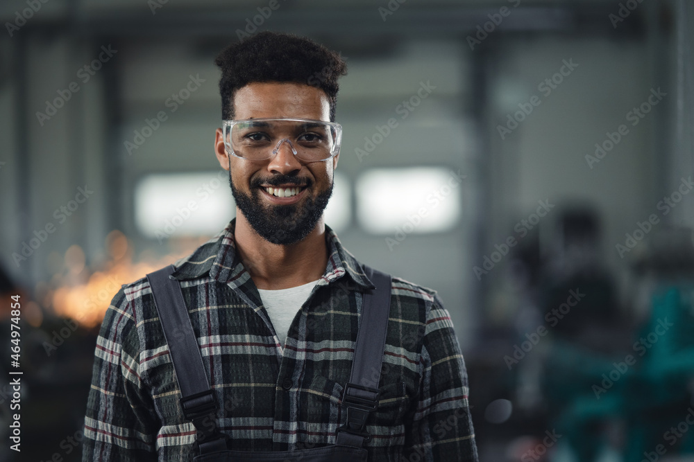 Wall mural Portrait of young industrial man working indoors in metal workshop, looking at camera.