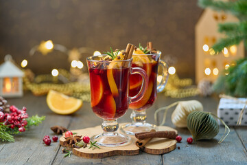 Two glasses of hot winter gluhwein. Alcohol red mulled wine with cardamom, cinnamon, clove, orange, cranberry, fir needles. Selective focus, blurred christmas decor background, horizontal