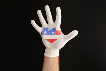 Patriotism. A man's hand in a white glove. A heart with an American flag on the glove. Black background. Copy space. The concept of national American holidays and voting
