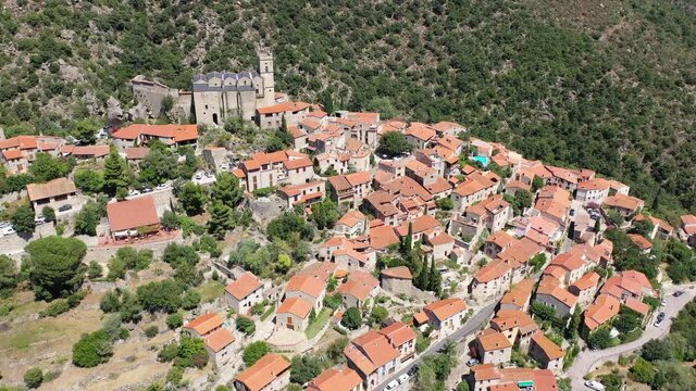 General summer view of picturesque French village of Eus in natural region of Conflent with tightly grouped houses, medieval church and castle ruins on top of hill