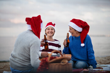 Senior couple with granddaugter with guitar celebrate New Year or Christmas and have picnic on beach.