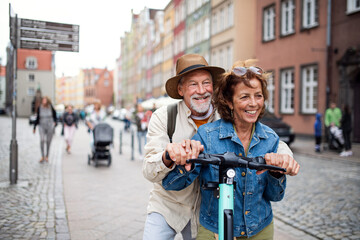 Portrait of happy senior couple tourists riding scooter together outdoors in town