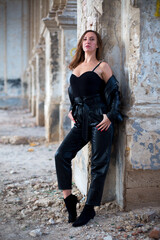 caucasian female in leather jacket and pants stay near an old brick column in a dilapidated catholic church