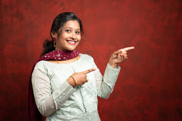 Happy smiling Indian woman Pointing finger to empty space by looking at camera - cocnept of showing offers or discounts for festival sales advertisement with copy space.