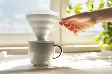 A female's hand removes a funnel with a filter from the cup. Alternative mothod of coffee brewing. Filter V60 with brewed ground coffee. Side view