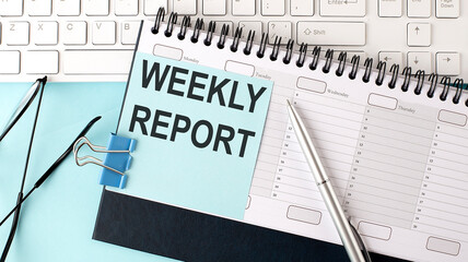 WEEKLY REPORT text on blue sticker on planning and keyboard,blue background