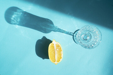 Top view of glass cap with lemon half on blue background. Sunny day with sharp shadows. Slimming...