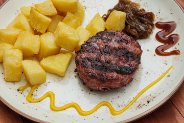 Grilled minced meat burger served with fried potato and caramelised onion on white dish.