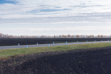 Rural asphalt road among the processed agricultural grounds against sky