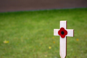 Red puppy flower placed on the small wooden cross in the green grass. Poppy remembrance day cross in a field