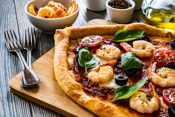 Pizza with prawns, mozzarella, cherry tomatoes and black olives on wooden table

