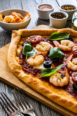 Pizza with prawns, mozzarella, cherry tomatoes and black olives on wooden table

