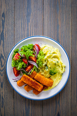 Fried fish sticks with potato puree and fresh vegetable salad on wooden table
