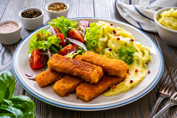 Fried fish sticks with potato puree and fresh vegetable salad on wooden table
