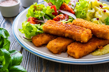 Fried fish sticks with potato puree and fresh vegetable salad on wooden table
