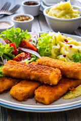 Fried fish sticks with potato puree and fresh vegetable salad on wooden table
