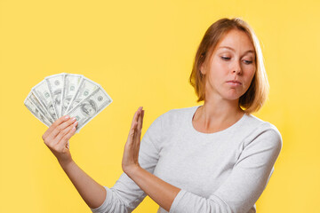 A serious woman holding a fan of dollars in her hand, and refusing them. Yellow background. The...
