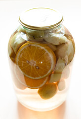 3-liter glass jar with homemade kompot (stewed fruit) made from sliced fresh apples and oranges close up on light brown table