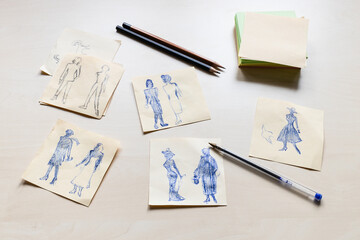 sketches of fashionable silhouette of woman of the XX century hand drawn on sheets of paper on light brown table