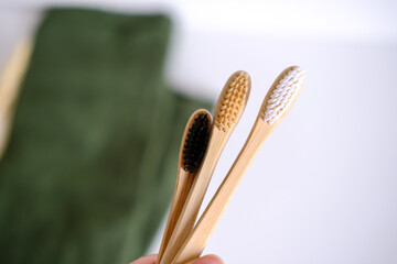 Three bamboo toothbrushes on a green towel with a plant on the background