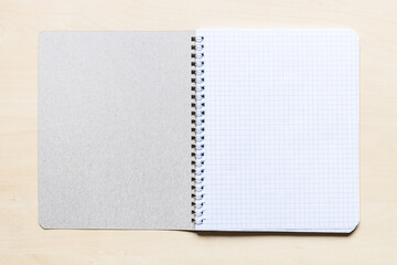 top view of first squared page of open blank spiral notebook on light brown wooden board