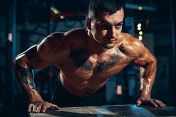 Close-up young man, muscled athlete, bodybuilder push-ups at sport gym, indoors. Concept of sport, activity, healthy lifestyle
