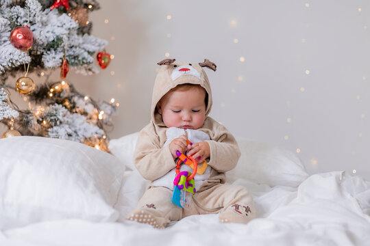 cute baby in a jumpsuit with deer horns playing with a colorful toy sitting near the Christmas tree. winter New Year's concept. educational toys, products for kids. space for text. High quality photo