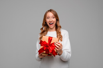 Fototapeta premium Beautiful young woman in white sweater holding in hands unboxed present and looking at camera with smiling broadly. Holidays, celebration and lifestyle concept
