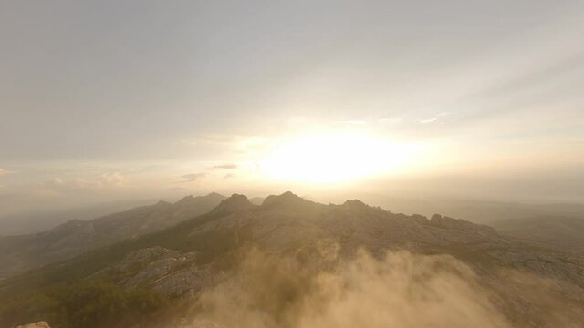 FPV video, mountain surfing, flying at high speed above the clouds with a granitic mountain range illuminated at sunrise. Mount Limbara (Monte Limbara) Tempio Pausania, Sardinia, Italy.
