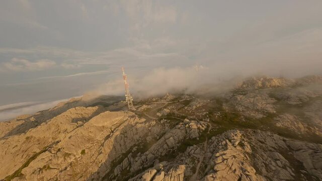 FPV video, mountain surfing, flying at high speed in the clouds with a granitic mountain range and an antenna farm during a beautiful sunrise. Mount Limbara (Monte Limbara) Tempio Pausania, Sardinia, 
