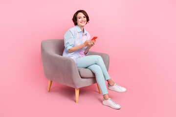 Fototapeta na wymiar Full length body size photo woman sitting in chair browsing internet on cellphone isolated pastel pink color background