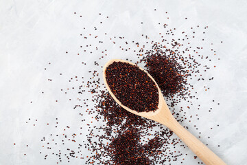 Ragi or black quinoa in wooden spoon on grey background, selective focus. Cereal is scattered on the surface of table