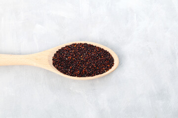 Black organic quinoa or Ragi,  millet seeds in wooden spoon, top view. Grey background, copy space