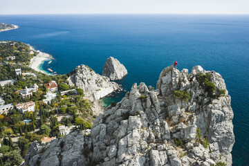 Aerial view of man tourist in red jacket standing on the rock top of cat mountain enjoying landscape of Simeiz with Diva and Penea rocks in background. Crimea