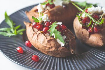 Whole baked sweet potato stuffed with quinoa, feta cheese, arugula and pomegranate on gray plate. Vegan food concept.
