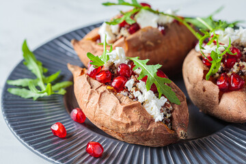 Whole baked sweet potato stuffed with quinoa, feta cheese, arugula and pomegranate on gray plate. Vegan food concept.