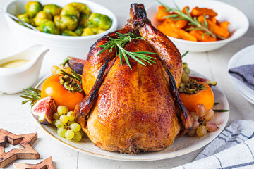 Roasted whole chicken served with fruits on plate, baked Brussels sprouts and carrots. Christmas or Thanksgiving food concept.