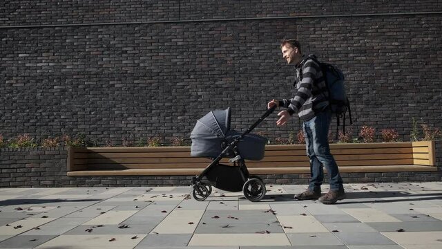 Father with newborn baby stroller meeting his little son and they walking together on the city near brick wall. Man in maternity leave with pram and child.