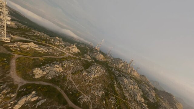 FPV video, mountain surfing, flying at high speed in the clouds with a granitic mountain range and an antenna farm during a beautiful sunrise. Mount Limbara (Monte Limbara) Tempio Pausania, Sardinia, 
