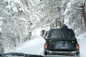 View from car window of caravan off-road vehicles driving along an extreme winter forest road. Extreme winter weather, sports, travel