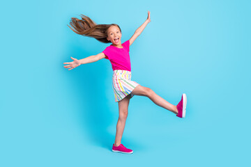 Fototapeta na wymiar Full size photo of cheerful young amazed happy girl raise hands leg fly hair isolated on blue color background