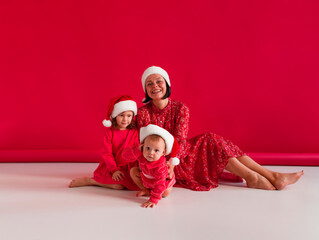 Fototapeta premium mom and two daughters in santa hats and red dresses