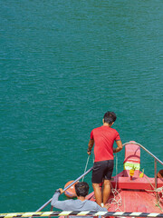 Top view of male crew prepared a rope to tie a buoy at bow of the ship before mooring at the shore of island. Happy casual tourism outside on tropical holiday destination. Cruise ship vacation.